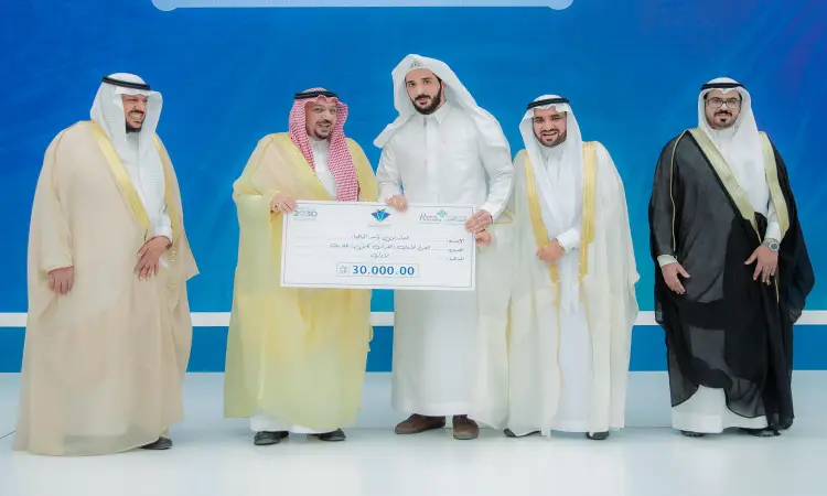 خمسة رجال تولي الزي السعودي التقليدي، يشمل الغترة أو الشماغ والعقال والبشت السعودي، الاتصالون على المنصة يتوسطهم صاحب السمو أمير منطقة القصيم. حضر اثنان منهم بشكل عماني رأسياً ثلاثة ألف ريال سعودي، وذلك من خلال فعاليات مسابقة حفظ القرآن الكريم التي تنظمها جامعة القصيم. يبدو الجميع مبتسمين ويقفون أمام خلفية تحمل لون أزرق أبيض.