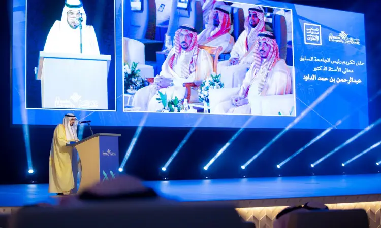 رجل يرتدي الغترة السعودية، والعقال، والبشت السعودي التقليدي، وقد عُرِّف بأنه أمير منطقة القصيم، وهو عادة ما يطلق على منصة الخطابة خلال تكريم في جامعة القصيم. اكتشفي شاشة كبيرة خلفه تم تصوير رئيس الجامعة وكوكبة من الشخصيات المهمة في تحقيق الهدف. ويغمر الملعب الأزرق في تكساس الفخم ويمنح الحدث قراءة قوية من اللق والهيبة.