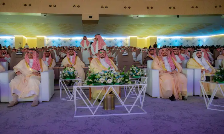يجتمع عدد كبير من الرجال الحاضرين الغترة أو الشماغ والعقال، مع البشت السعودي، في قاعة مؤتمرات حفل رحبة ومضيئة، لحضور تكريم رسمي في القصيم. تتزين القاعة ب المكتبات القديمة ويتليها القديمة الزهرية. ومن بين الحضور صاحب السمو أمير منطقة القصيم.