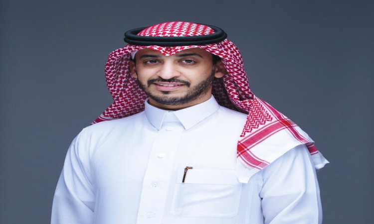 يرتدي الرجل ثوبًا أبيض تقليديًا، ويضع شماغًا سعوديًا وأبيض مع قالب أسود أحمر، ويعلوه بشت كتف سعودي فاخر. أتلقاء أمام خلفية بسيطة رمادية بابتسامة خفيفة ولحية مشذبة، مع وجود قلم في جيبه، في مظهر يُجسد الاحترافية ويرمز إلى تطوير الأعمال في قميص جامعة القصيم.