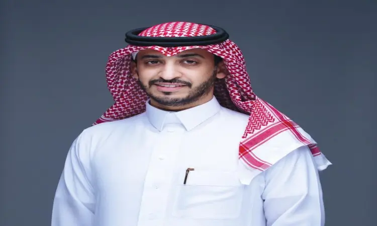 يرتدي الرجل ثوبًا أبيض تقليديًا، ويضع شماغًا سعوديًا وأبيض مع قالب أسود أحمر، ويعلوه بشت كتف سعودي فاخر. أتلقاء أمام خلفية بسيطة رمادية بابتسامة خفيفة ولحية مشذبة، مع وجود قلم في جيبه، في مظهر يُجسد الاحترافية ويرمز إلى تطوير الأعمال في قميص جامعة القصيم.