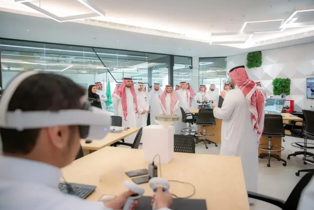 The contact group of men, dressed in a Saudi Arabian ghutra or shemagh with an aqal and a Saudi bisht, are part of the Digital Digital Digital Government Authority, in a modern office with bright lighting and a modern design. It is characterized by discomfort, as one of the men sets up a virtual reality device on the table in front of him.