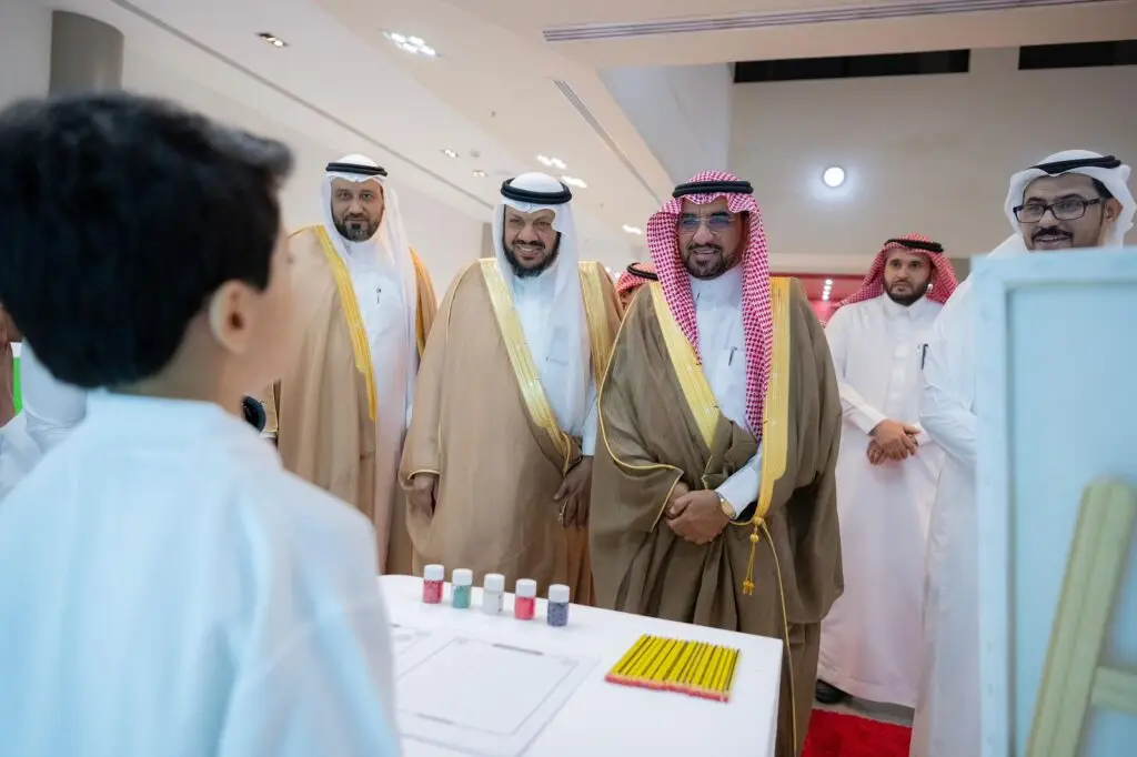 الاتصال بمجموعة من الرجال مرتدين الغترة والشماع والعقال والبشت السعودي، وهم يبتسمون ويشاهدون باهتمام أحد لآخرين من الفعالية، وهو فتى صغير الاتصال أمام شاشة تعرض زجاجة وأقلام رصاص، وذلك من خلال فعالية أُقيمت في النادي الصيفي السابع عند القصيم.