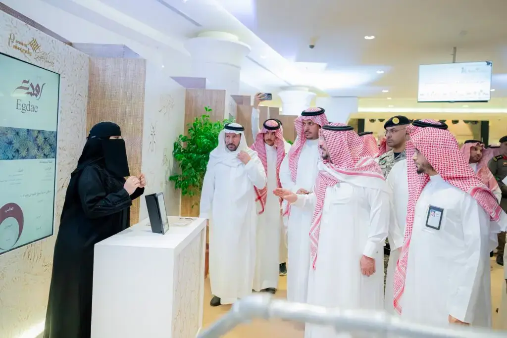 In the university gallery, a group of men wearing a ghutra or shemagh, an aqqal and a Saudi bisht connect with a woman, dressed in a black abaya and niqab, listening intently to a presentation in one of the interior corners. Security men are seen in the background during the event highlighting the Buraydah Dates Carnival.