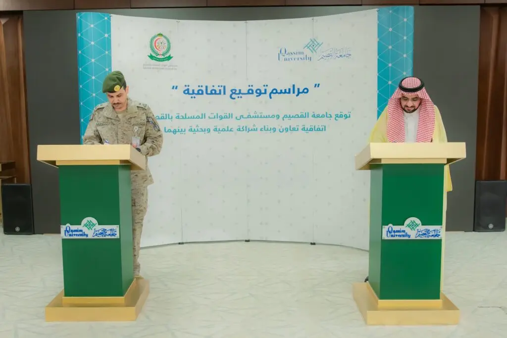 كات ضابط عسكري إلى جانب يرتدي رجل البشت السعودي والغترة والعقال، وكلهم في منصة رسمية، حيث يقومان بتوقيع مخصص للتعاون. وتحمل في الخلفية لوحة تحمل نصوصًا عربية وشعارات مستشفى القوات المسلحة، بالإضافة إلى شعار جامعة القصيم الرسمي.