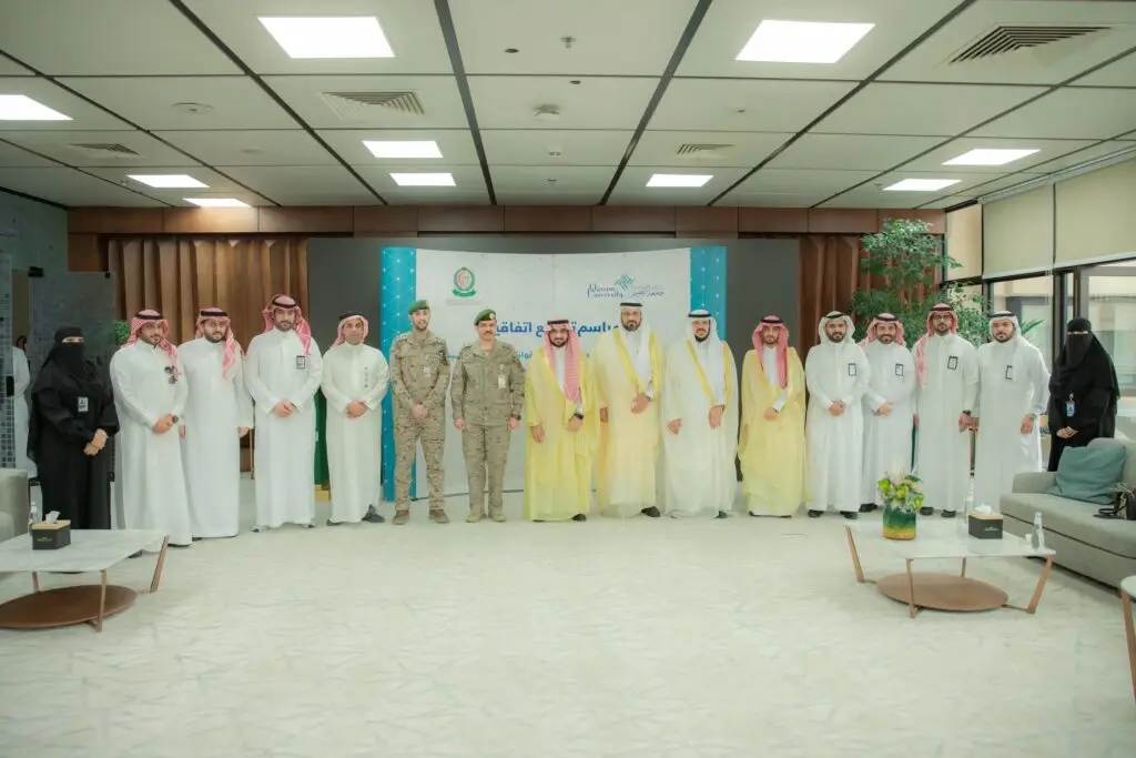 مجموعة من الرجال الحاضرين الغترة أو الشماغ والعقال والبشت السعودي، بالإضافة إلى عدد من القوات المسلحة من سوبلي بزيهم، وكوكبة من بالعباءات وقفن جميعاً مصطفين في صف تحت إحدى القاعات وصورة تذكارية. وأشار في الخلفية إلى بانر عبارة عن فترة باللغة العربية تُبرز "التعاون العلمي بين جامعة القصيم ومستشفى القوات المسلحة بالقصيم".