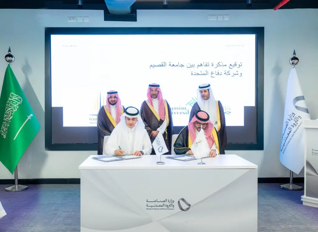 يجلس رجلان على طاولة الرجال ويوقعان وثيقة وثيقة بأنظمة الطائرات بدون طيار، بينما يلمسان خلفهما ثلاثة طواحين بالغترة أو الشماغ السعودي مع العقال والبشت السعودي، في مشهد يعكس الطابع الرسمي للفعالية. ويظهر في العلم السعودي وشاشة رقمية تحمل نصوصاً باللغة العربية، بما في ذلك يبرز الرسمية لهذا الحدث الذي ساعده جامعة القصيم.