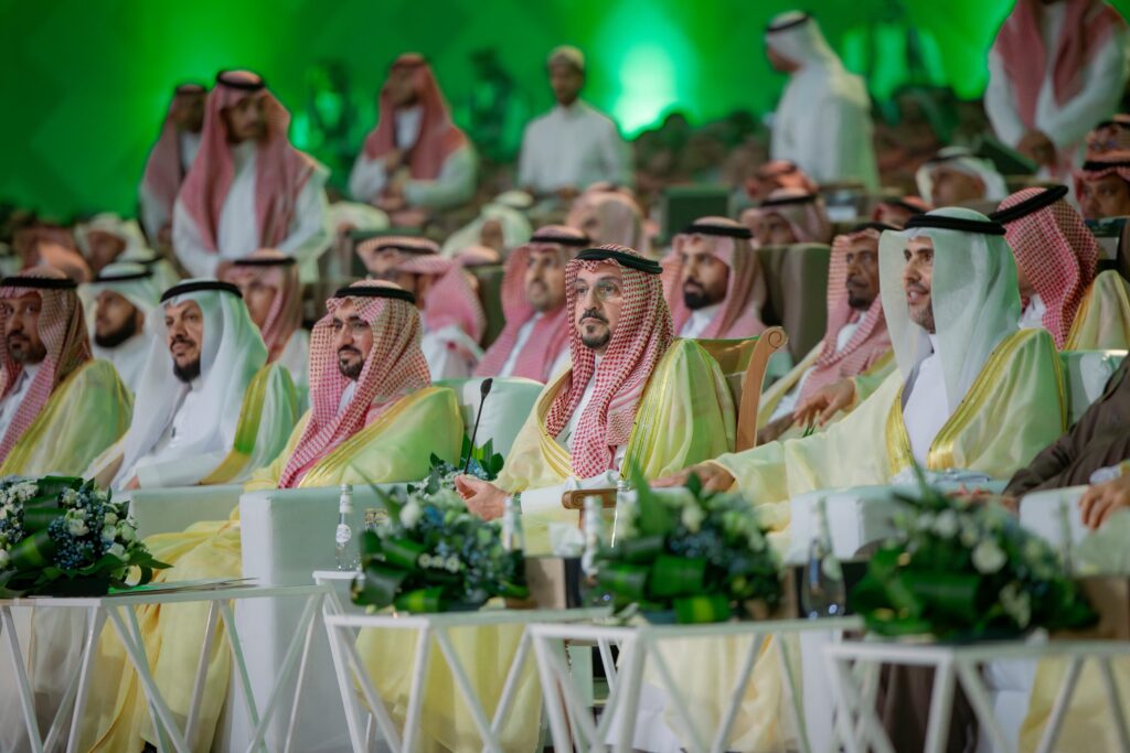 يجلس مجموعة من الرجال مرتدين الغترة أو الشماغ والعقال والبشت السعودي في مقابل مساهمته في الحياة اليومية في جامعة القصيم، ويحيط بهم إضاءة وزينة احتفاء بمناسبة اليوم الوطني 94، وذلك بحضور جمهور يظهر في الخلفية.