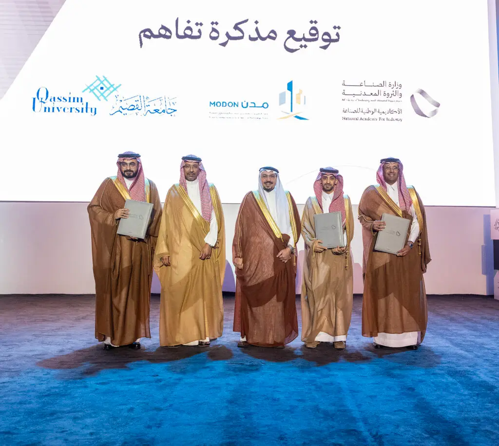 القطة خمسة رجال مرتدين الغترة أو الشماغ السعودي مع العقال، وبعضهم يرتدي البشت السعودي، على تيست حاملين وثائقي رجالي، ليلتقطوا صورة جماعية أمام خلفية تحمل شعارات جامعة القصيم والهيئة السعودية للمدن الصناعية والأكاديمية الوطنية للصناعة وعدد الفرق من الأخرى.