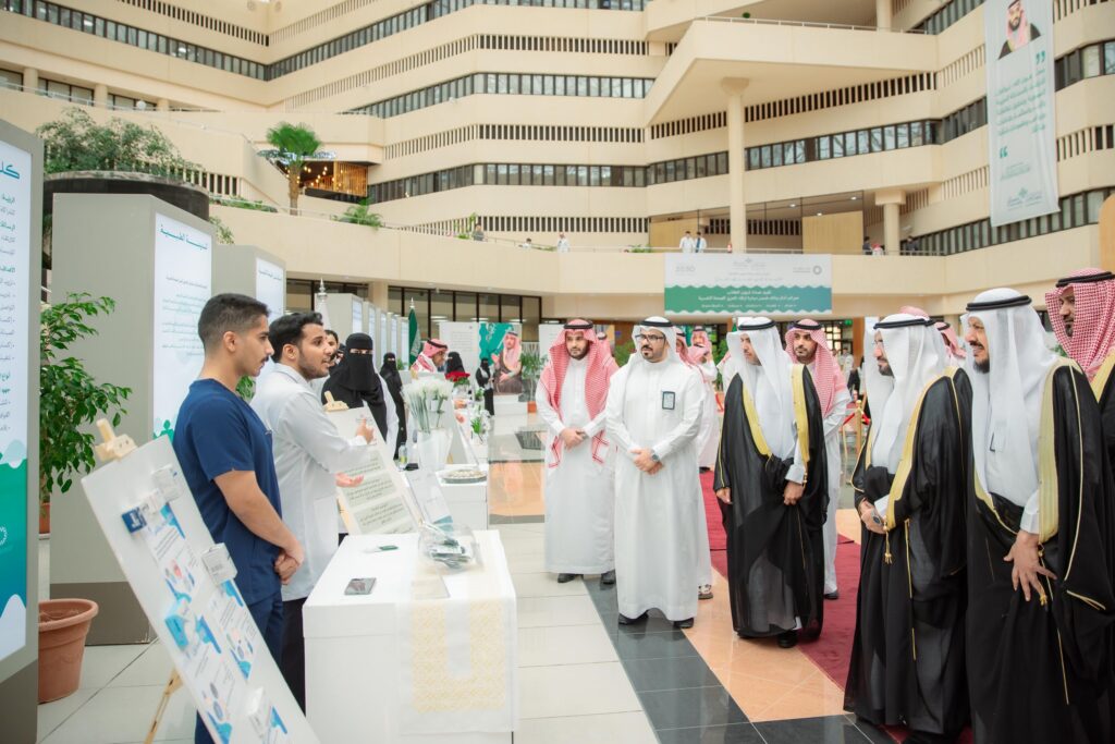 يجتمع مجموعة من الرجال، يتقدمون رئيس الجامعة، حيث يجتمعون الغترة والعقال والبشتاء السعودي، إذ سيرتدون والزي الطبي الرسمي. يتفاعلون مع فعاليات معرض آمال الصحة النفسية في مبنى حديث وواسع، مستعرضين الأركان التعريفية واللوحات التوعوية الموزعة في أرجاء المعرض.