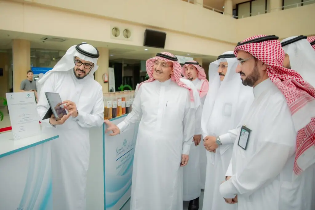 مجموعة من الرجال تولي الزي السعودي الأصلي، بما في ذلك الشماغ أو الغترة داخل السعودية، يجتمعون حول منصة عرض إحدى المنظمات العامة أو المعارض، حيث يقوم باختيار محتوى على جهاز لوحي أمام الآخرين، وذلك في إطار إبراز جهود الشراكات المجتمعية لجامعة القصيم.