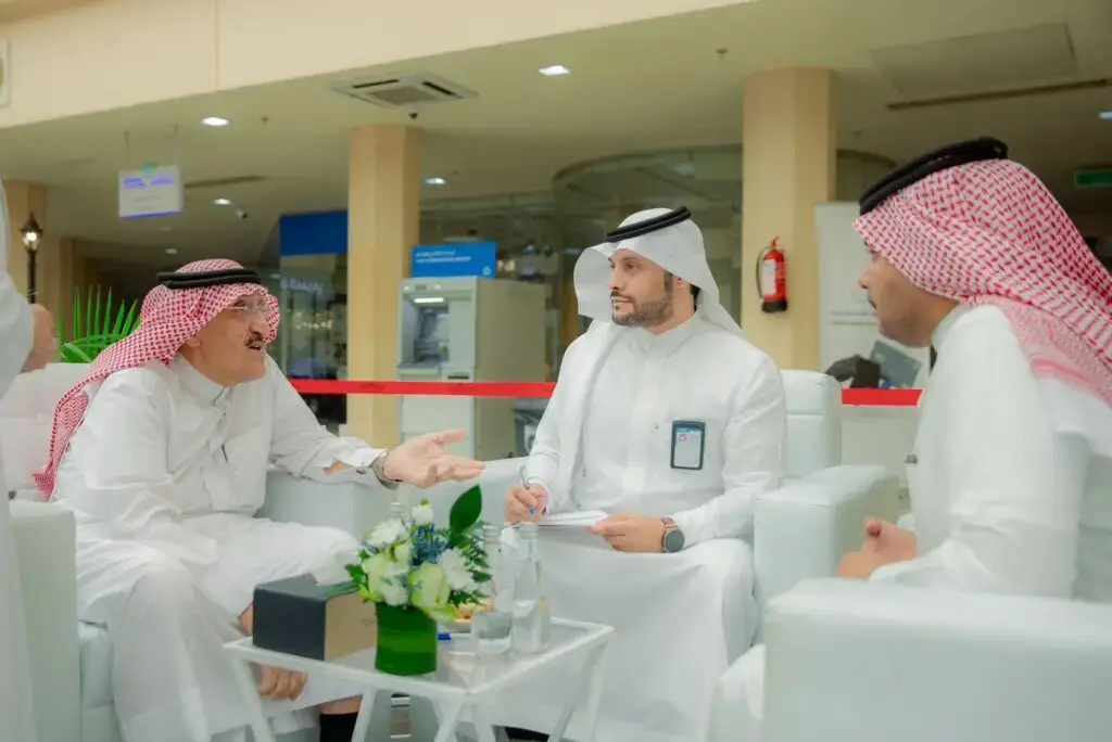 يرتدي ثلاثة رجال الزي السعودي الأصلي، يشمل الشماغ أو الغترة السعودية، ويتبادلون الحديث حول طاولة صغيرة مزينة بالزهور وبوات المياه، وذلك في بيئة داخلية حديثة. يقوم أحد بالإشارة أثناء النقاش بينما يدون آخر ملاحظة حول فكرة، وذلك خلال مناقشتهم لموضوع الشراكات المجتمعية مع الهيئات الحكومية في إطار رسمي يخص جامعة القصيم.