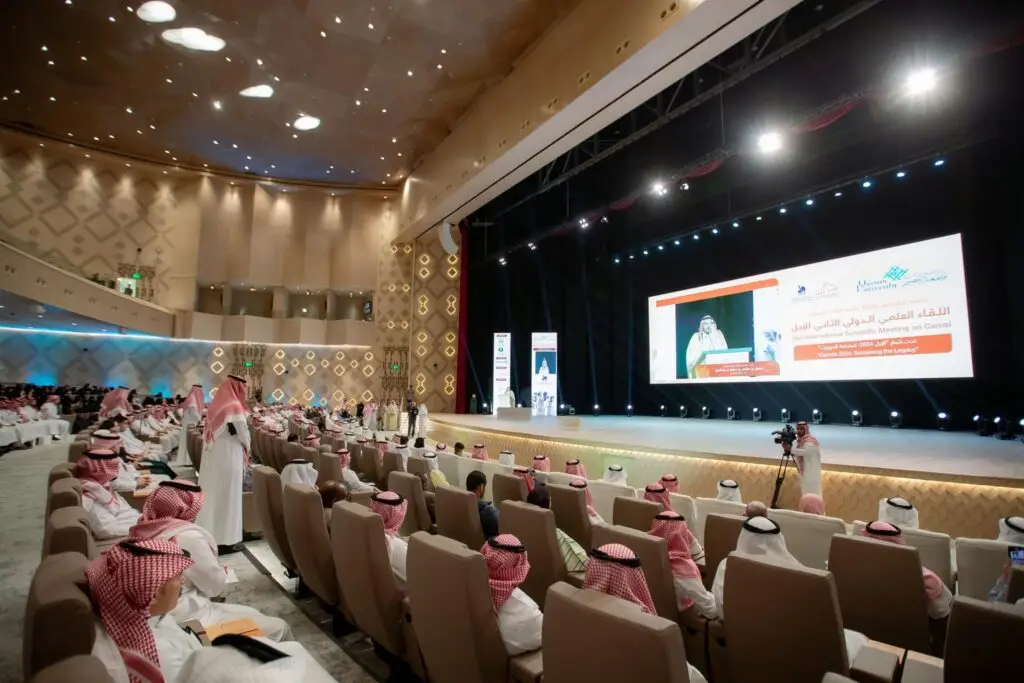 اكتظ المدرج في جامعة القصيم بالحضور، حيث يرتدي الجميع الشماغ السعودي أو الغترة السعودية، ويتابعون باهتمام كلمة الكشف عن الحضور خلال اللقاء العلمي الدولي للإبل. وقد عُرضت صورة واضحة ونصوص باللغة العربية على شاشة كبيرة ولطيفة، وسط إضاءة ساطعة وتصميم داخلي حديث يليق بمكانة الجامعة.