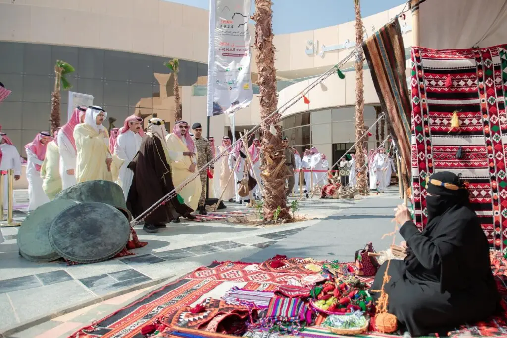 تجلس امرأة ترتدي زيًا تقليديًا على سجادة مزخرفة، وحولها مشغولة يدوية، وبجوارها عدد من الحفاضات. وتولى مجموعة من الرجال الثياب البيضاء والبنية مع الشماغ أو الغترة السعودية، يتقدمهم أمير منطقة القصيم، ليتمكن من العرض الثقافي المنظم من قبل جامعة القصيم.