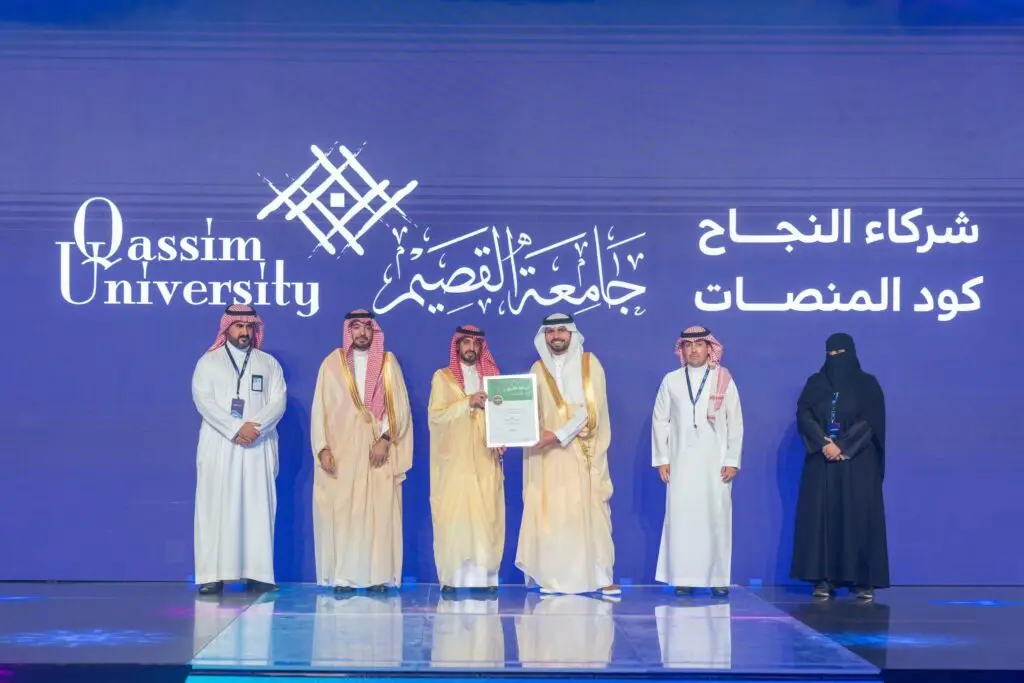 Six people on a podium at Qassim University struggled to face the Saudi shemagh, or Saudi ghitra, when wearing costumes. After some time, a text in Arabic and English on the back screen reads "Platform Code."