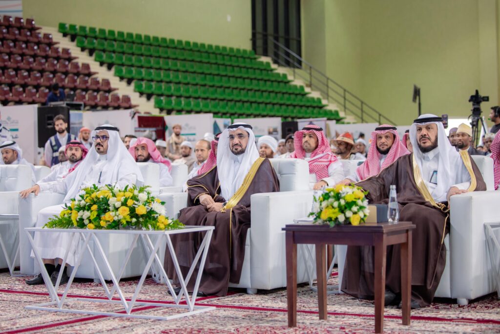 يجلس مجموعة من الرجال مرتدين الغترة أو الشماغ والعقال والبشتاء السعوديين، يتقدمهم رئيس الجامعة، على كراسٍ رابعًا رابعًا خلال فعالية داخلية في جامعة القصيم. وتزين الجداول أمامهم التنسيقات الزهرية، بينما يظهر خلفهم صفوف الحضور من الاستماع والجمهور.