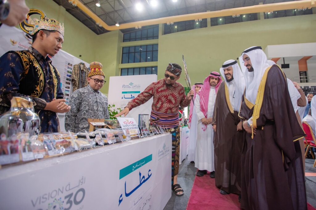 وقف عدد من الرجال بزيهم التقليدي، مرتدين الشماغ والعقال والبشت السعودي، حول جناح خاص في معرض داخلي مُعد عطاء. وقد عرض مصنع التنين مجموعة من المنتجات، وسطه شعار رؤية السعودية 2030. ويوضح أحد الحضور بعض العروضات بإيماءة منه، تابع الآخرين باهتمام وابتساماتهم تعلو وجوههم، يتقدمهم رئيس جامعة القصيم.