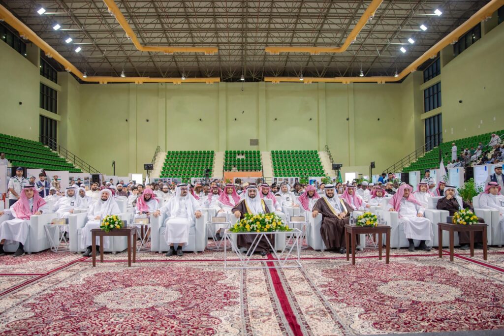 جلسة جمع كبيرة من رجال مرتدين الغترة أو الشماغ السعودي مع العقال، وبعضهم متوشحون بالشت السعودي، على مقاعد ثلاثية في قاعة كاملة تتخللها مقاعد خضراء وسجاد أحمر بنقشية تقليدية. جاء ذلك ضمن الفعالية في القصيم لتكريم الطلاب الأساسيين، وذلك تحت رعاية رئيس الجامعة الرئيسي وإطار برنامج عطاء.