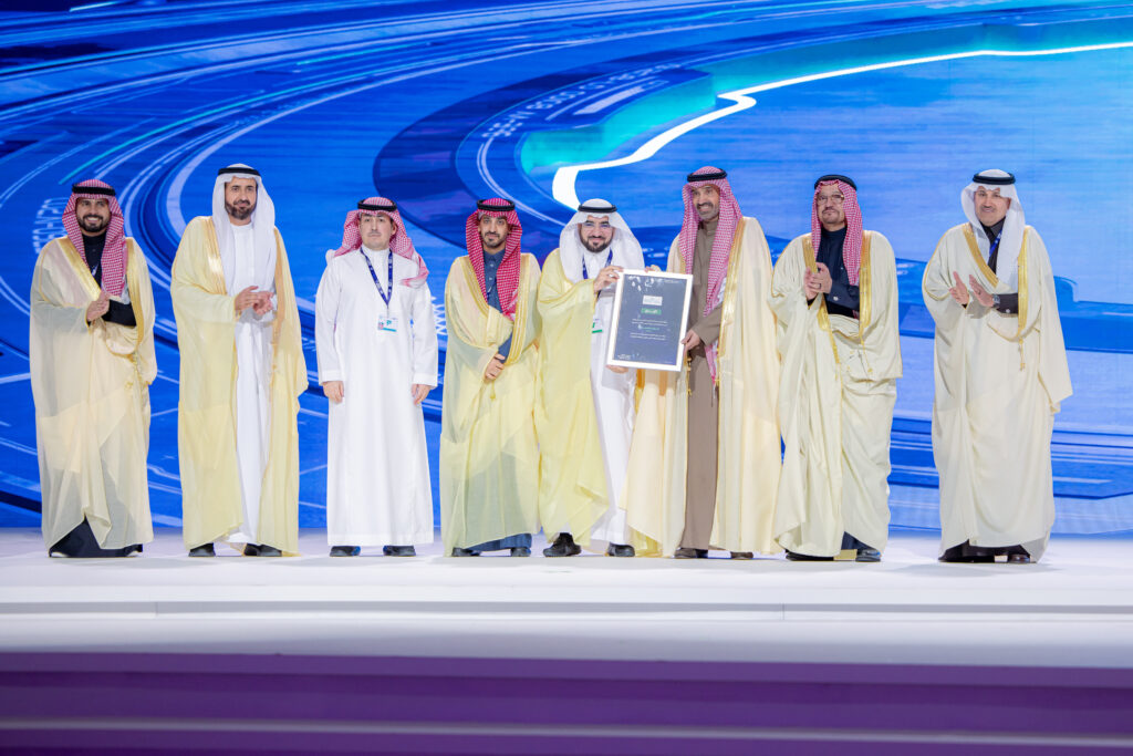 أت مجموعة من الرجال مرتدين الغترة أو الشماغ والعقال، بالإضافة إلى البشت السعودي، على منصة في جامعة القصيم، حيث يقوم أحد بحمل درعٍ مُؤطَّر تكريمًا لجهودهم في التحول الرقمي. اخترعت تهمهم على شاشة رقمية ضخمة، رسم كاريكاتوري ت تختولها وخطوط حديثة بتقنية تقنية حديثة، بينما يبتسمون ويلتقط لهم الصورة المصوّرة تبرز للمرة الأولى لتحقيق هدفها.