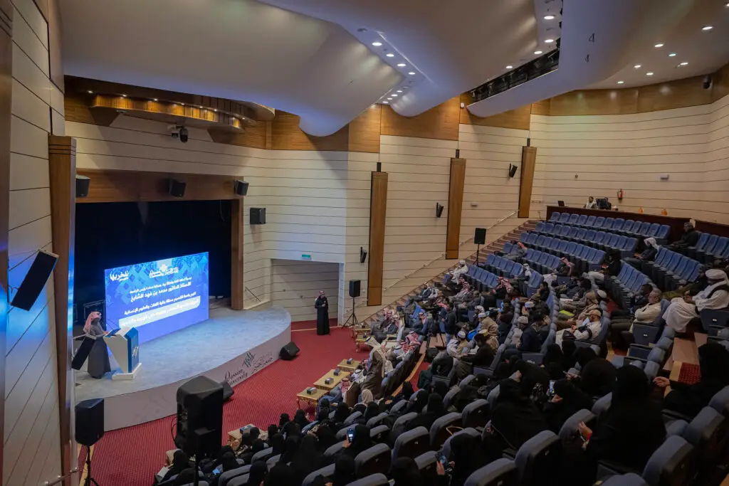 اتصل بالمنصة في قاعة المحاضرات الحديثة في القصيم، بجانبه شاشة رقمية كبيرة تعرض نصوصًا ورسومًا وليس. ويحضُر الفعاليّة جمع من الحاضرين الشماغ السعودي أو الغترة السعودية، ويوثيقة العنصر السبب الحقيقي لقاطع الصور. تأتي هذه الأمثلة احتفاءً باللغة العربية وبيومها العالمي.