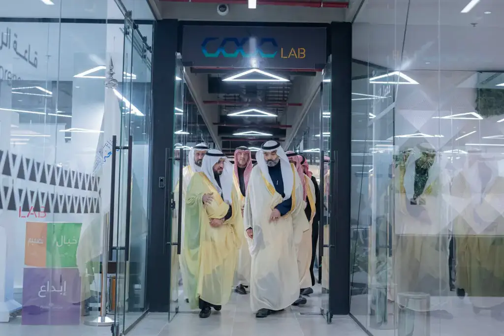 اجتمعوا من الرجال مرتدين الزي السعودي التقليدي، بما في ذلك ممثل من وزارة الاتصالات، وتوافقوا عبر الأبواب الزجاجية لمكتب عصر حديث باسم "CAVE LAB"، ضمن المجالات المتميزة والمضيئة التي تخصصتها جامعة القصيم للبحث فقط.