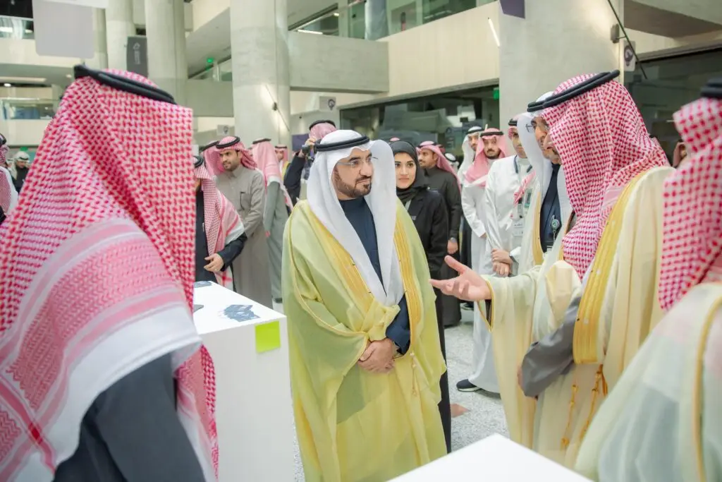 يجتمع مجموعة من الرجال الزي السعودي الأصلي، بما في ذلك الثوب والشماغ أو الغترة داخل السعودية، أحد الأشخاص، ويتبادلون النقاش حول المسائل المتعلقة بالصناعة والثروة المعدنية، وذلك ضمن فعالية أو معرض نظمته جامعة القصيم للأطفال.