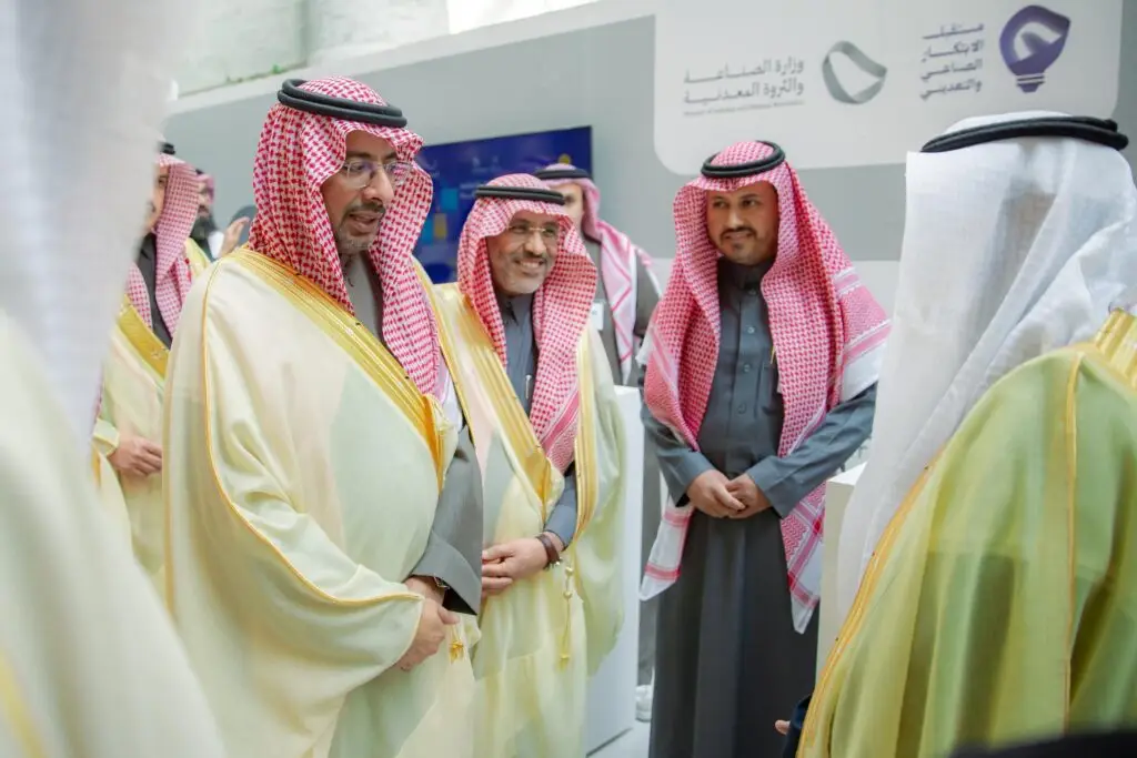 الاتصال مجموعة من الرجال مرتدين الزي السعودي الأصلي، والذي يشمل الثياب والشماغ السعودي الأحمر داخل، ويتبادلون الحديث فعالية مقامة في مكان مغلق تُعنى بالصناعة والمبتكرين، حيث لاحظت ملاحظة باللغة العربية في الخلفية.