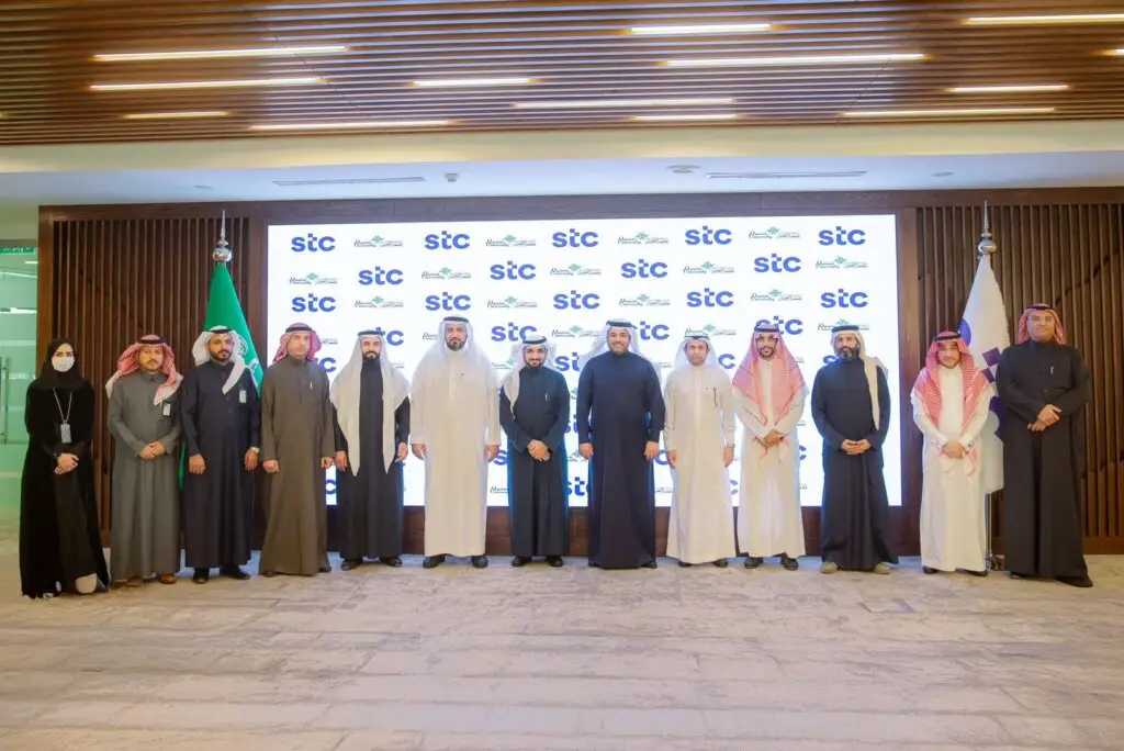 ستة أشخاص، من بينهم الرجال الحضور السعودي الرسمي الامتداد في الشماغ أو الغترة السعودية، ونساء يرتدين أزياء رسمية، في صف واحد أمام خلفية تحمل شعارات مجموعة STC والأعلام. مبادرة هذه الصورة لمراسم توقيع مذكرة بين مجموعة STC وجامعة القصيم.