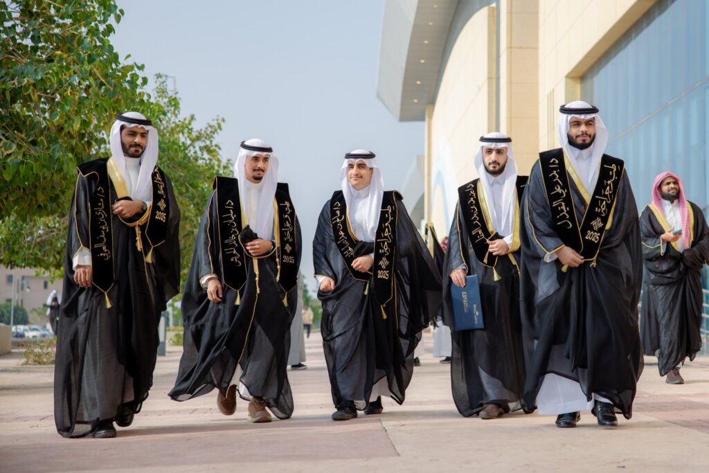 مجموعة من الرجال الذين تولى الغترة السعودية أو الشماغ والعقال، بالإضافة إلى البشت السعودي و تحررات الرسمية، من بينهم أحد خريجي جامعة القصيم، يسيرون في الهواء الطلق تحت من مبنى عصري وهم يبتسمون ويحملون ملفات بأيديهم، للتكتل على ترخيصهم.