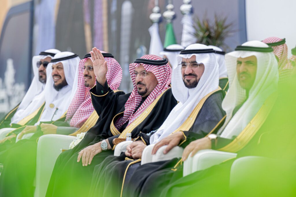 يجلس مجموعة من الرجال مرتدين الغترة أو الشماغ والعقال والبشت السعودي في صف واحد، يتوسطهم أمير منطقة القصيم الذي يرفع يده بالتحية. لتشجيع أعلام الجامعة والنباتات على تزين المكان، تضفي في وقت لاحق الخلفية الكافية لأوراق الشجر الخضراء طابعًا مميزًا على متفجرات الموظفين الحكوميين.