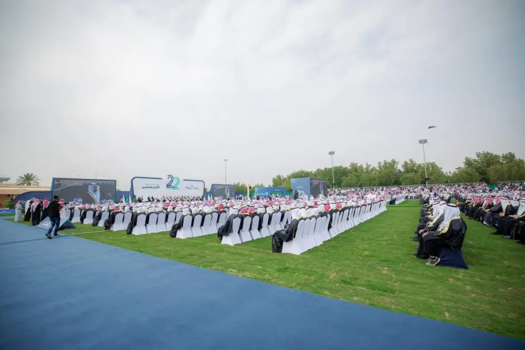 خارجي كبير يجمع عدداً غفيراً من الحضور، يجلسون في كتابهم على خلفية قماشية، ويشتركون في المشاركة والزي السعودي التقليدي، الممسولون في الثوب والشماغ أو الغترة السعودية. تزين المكان لافتة وشاشات ضخمة تحتفي بخريجي الجامعة، ويشرف الشرف برفقة صاحب السمو الأمير منطقة القصيم، وذلك حتى يدخل إليها طقس الغائم.