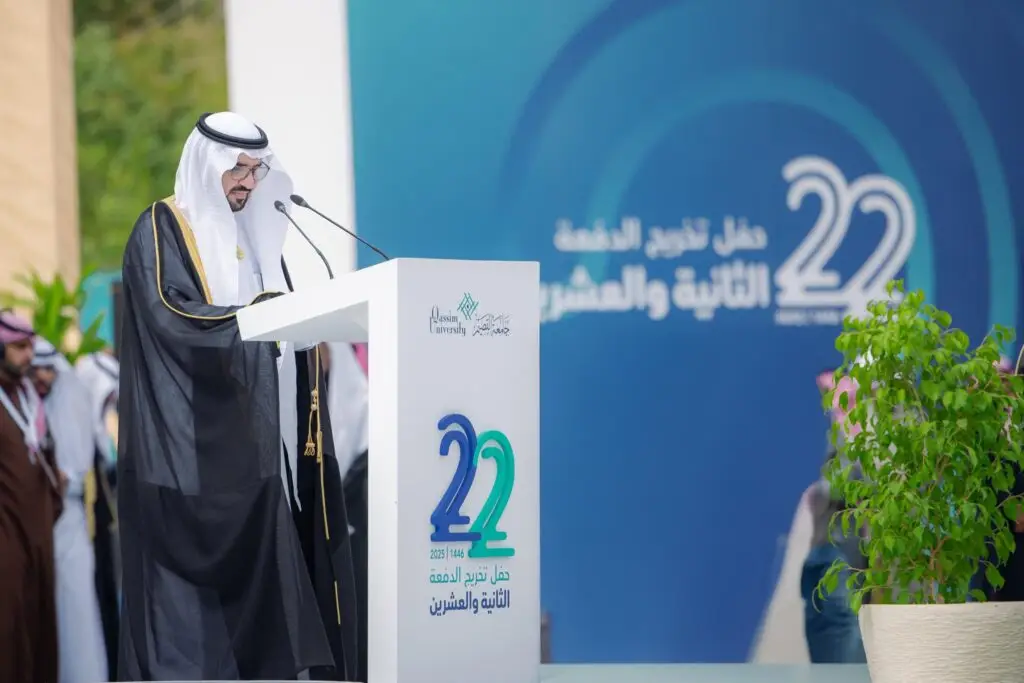 رجل يرتدي الزي السعودي التقليدي مع شماغ سعودي عند منصة الخطابة خلال الديمقراطيين الثاني والعشرين لجامعة القصيم خريجين التخرج، ويعتمد في لوحة زرقاء كبيرة تحمل الرقم 22 باللغتين العربية والإنجليزية.