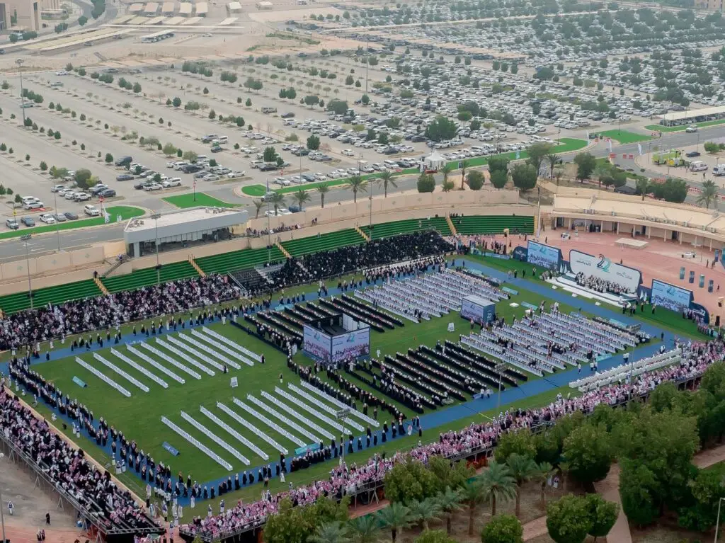 يحتشد جمع غفير في إستاد خارجي واسع، حيث تصطف صفوف الحضور من الحضور المتميزين، ومن بينهم العديد من الشماغ السعودي أو الغترة السعودية، حضور في التخرج منظم ينظمه جامعة القصيم. وتوقفت عن البحث عن خطوط حمراء لسيارات تنفيسة لمساحة خضراء منسقة وأشجار باسقة، مما يضفي على أهدافها الرسمية رسمياً ومهيباً.