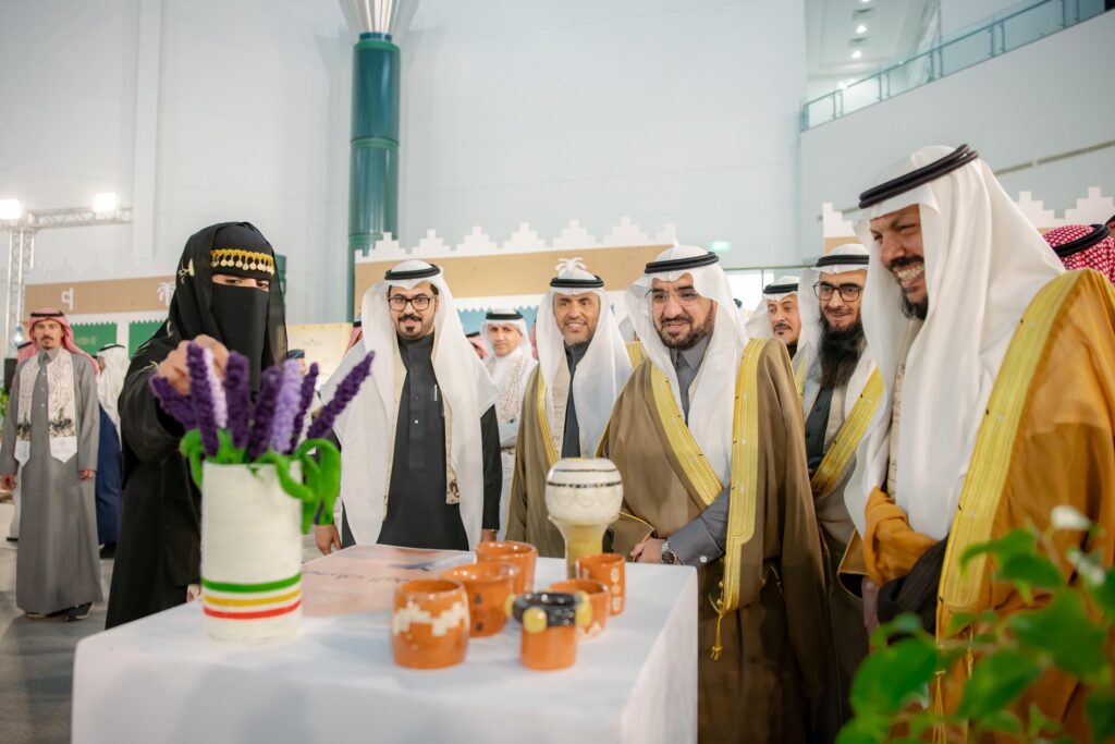 يجتمع عدد من الرجال مرتدين الشماغ السعودي والعقال والبشت السعودي، ويبتسمون خلال مشاهدتهم سيدة الفخارية وعليها الالتزام بالأعضاء، وذلك في معرض داخلي نظمته جامعة القصيم. وتتضمن مجموعة متنوعة من القطع الخزفية بالإضافة إلى مزهرية تحتوي على زهور بنفسجية.