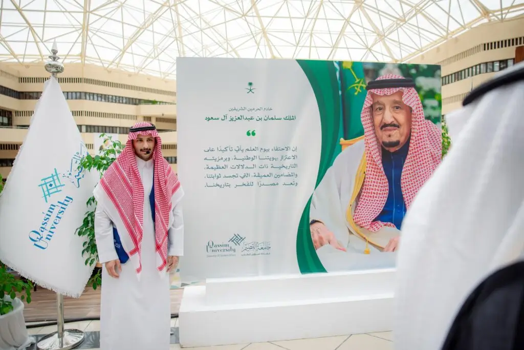 رجل يرتدي الزي السعودي التقليدي، شاملاً الشماغ أو الغترة السعودية، بجانب لوحة كبيرة تحمل صورة الخادم الحرمين الشريفين الملك سلمان بن عبدالعزيز آل سعود، وذلك ضمن فعالية السيدات أقامتها جامعة القصيم احتفاءً بيوم العلم. كتب في نسيج الشعر الوطني والنص العربي بوضوح في ما يلي لتغطيه أسقف.