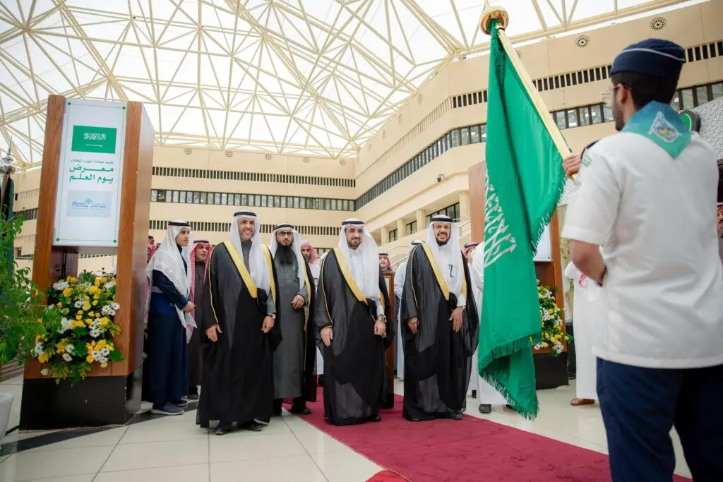 يسير مجموعة من الرجال بزي سعودي تقليدي، تمسك الشماغ أو الغترة السعودية، على سجادة حمراء حمراء، وهم يبتسمون ويتبعون أحد الكشافة الذي عصر علم المملكة العربية السعودية، قوية بيوم العلم. وتتميز المبنى بنوافذه هناك وتنسيقاته الزهرية.