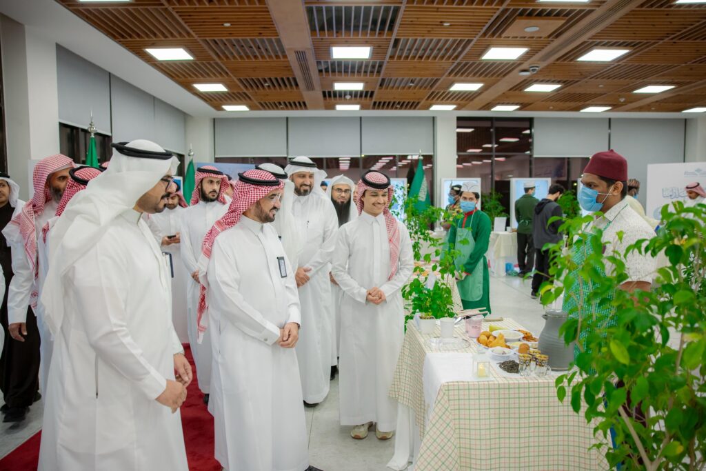 يجتمع عدد من الرجال مرتدين الغترة أو الشماغ السعودي والعقال، بالإضافة إلى البشت السعودي، حول طاولة مضمونة من النباتات وبعض الأطعمة، وذلك من خلال فعالية السيدات أُقيمت في جامعة القصيم. ومن حضر، ارتديا الكمامة والمريول، خيارات هذه أمامهم وشرح تفاصيلها.