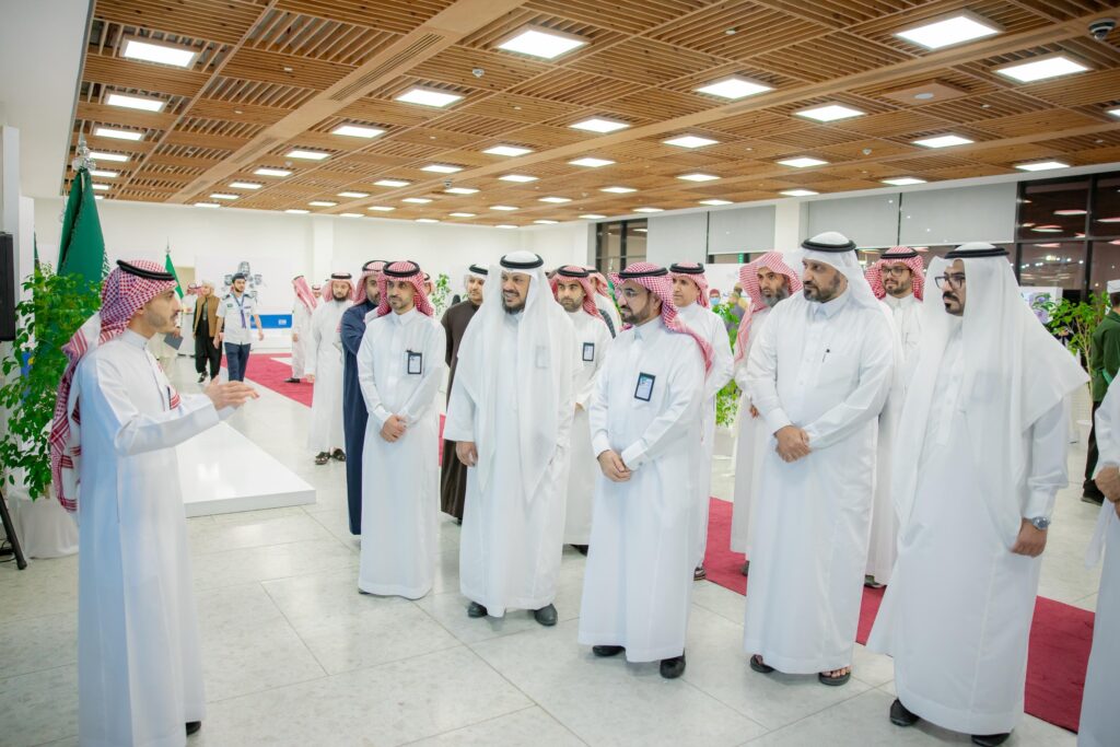 يجتمع عدد من الرجال مرتدين الغترة السعودية والعقال والبشت السعودي أحد داخل مباني جامعة القصيم، حيث يجتمعون مع بوقار ويستمعون باهتمام كبير. يتميز العقار بتصميم مميز بإضاءة حديثة ونباتات طبيعية وسجادة باللون الأحمر، مما يشير إلى التوقيع الرسمي للمناسبة.