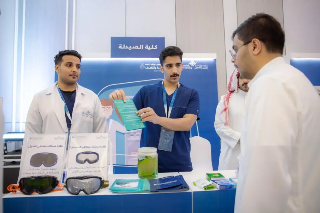 كل ثلاثة رجال غترة سعودية، عقال، وبشت سعودي رسمي في جناح كلية الصيدلة في القصيم لغرض تعزيز الصحة والتثقيف. وهو أحد بشرح تعريفي لزائر يهم، بينما تُعرض على طبي خاص وبعض الكتيبات التوعوية ووراء طبية.