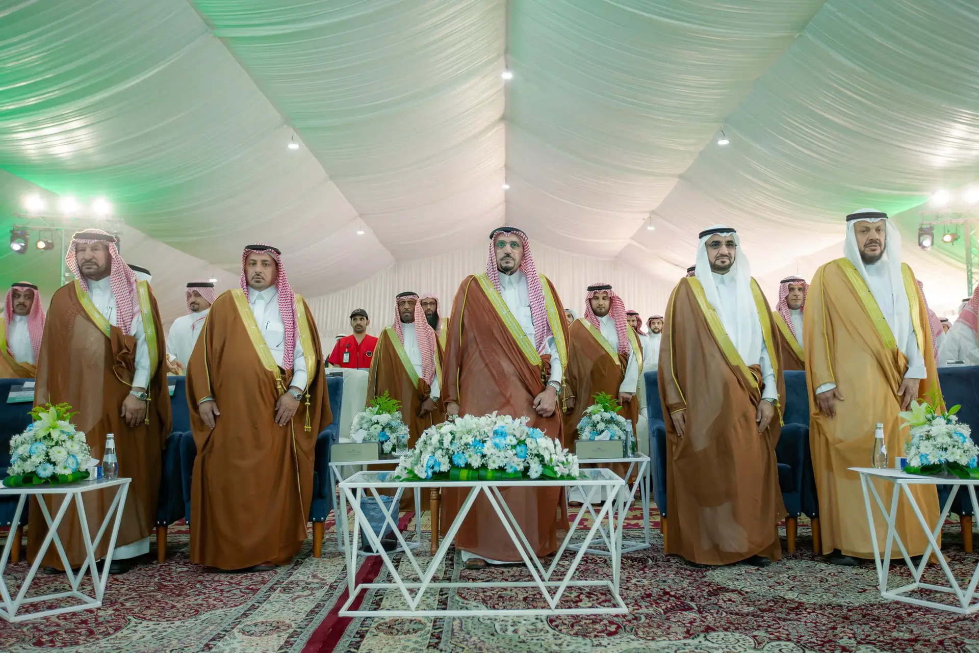 وقفة مجموعة من الرجال مرتدين الغترة أو الشماغ والعقال، أخذوا يعبرون البشت السعودي، خيمة مزينة بالستائر بيضاء وتنسيقات زهور وسجاد مزخرفة، وذلك خلال مراسم حضرها صاحب السمو أمير منطقة القصيم ضمن فعاليات حملة الجامعة الشاملة في محافظة النبهانية.
