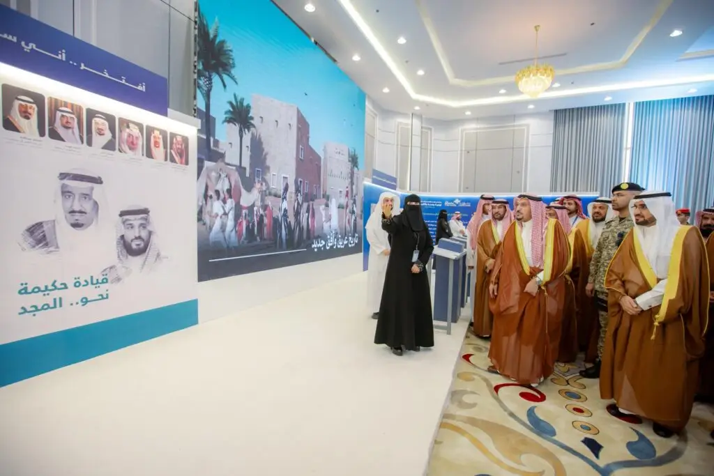 مجموعة من الرجال الذين يرتدون الغترة السعودية أو الشماغ والعقال والبشت السعودي، إلى جانب فتاة ترتدي عباة، الاتصالون في قاعة عرض حديثة في محافظة النبهانية، لأجل دون لوحة كبيرة تتضمن صوراً لقيادات المملكة العربية السعودية، وذلك ضمن فعاليات حملة الجامعة الشاملة التي تنظمها جامعة القصيم.