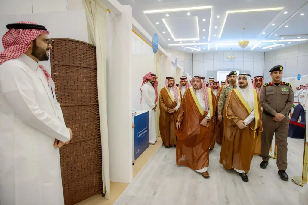 مجموعة من الرجال السعوديين الحاضرين الغترة والعقال والبشت السعودي، سيشون في رواق حديث ومضيء بمحافظة النبهانية، برفقة أحد الضباط الرسميين. ويقف أحد الحضور مرتديًا الثوب الأبيض والشماغ السعودي إلى جانب أحد الحواجز، تابعوا فعاليات حملة الجامعة الشاملة في القصيم.
