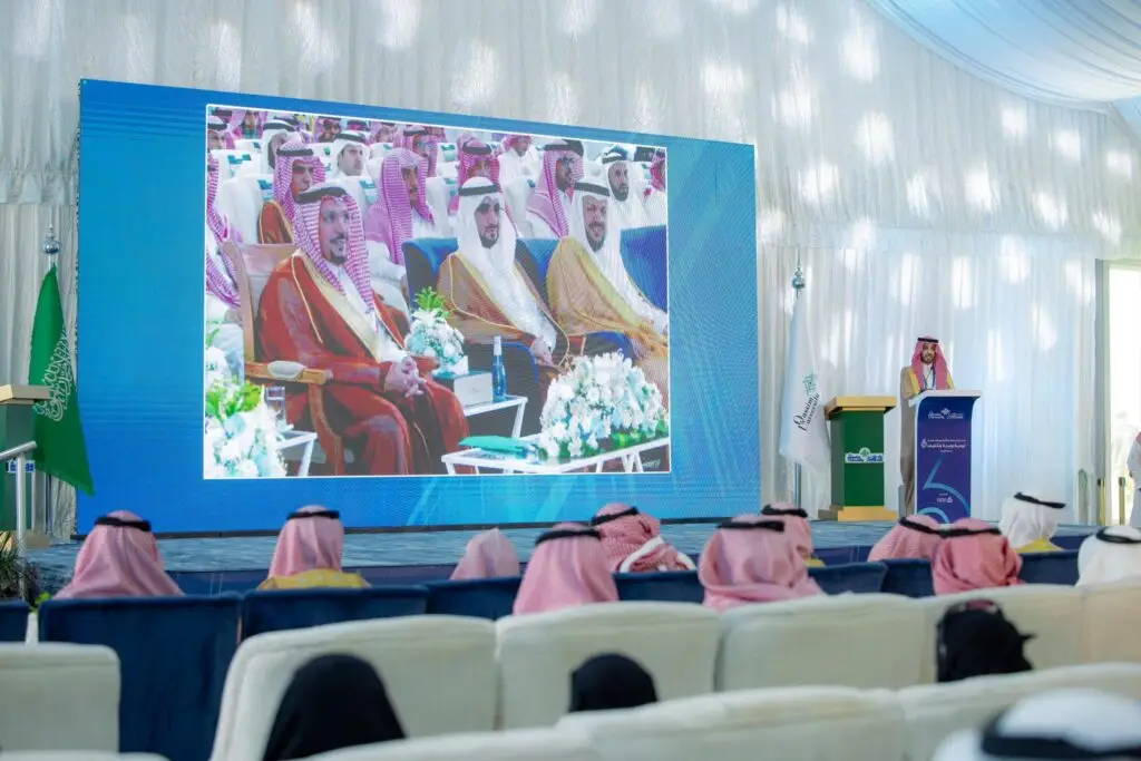 يتحدث واحد فقط من على منصة الخطابة أمام الحضور في خيمة واسعة لحملة الجامعة الشاملة، حيث يظهر خلفه شاشة كبيرة تعرض صورًا لمسؤولين سعوديين وصاحب السمو أمير منطقة القصيم أثناء الحضور المقامة في مقاطعة النبهانية. وظهرت أعلام المملكة العربية السعودية وستائر جزئية كاملة المكان، بينما يبرز عدد من الحضور مرتدين الغترة أو الشماغ مع العقال والبشت السعودي بما في ذلك دقة الهوية الوطنية وروح الشرعية الرسمية لجامعة القصيم.
