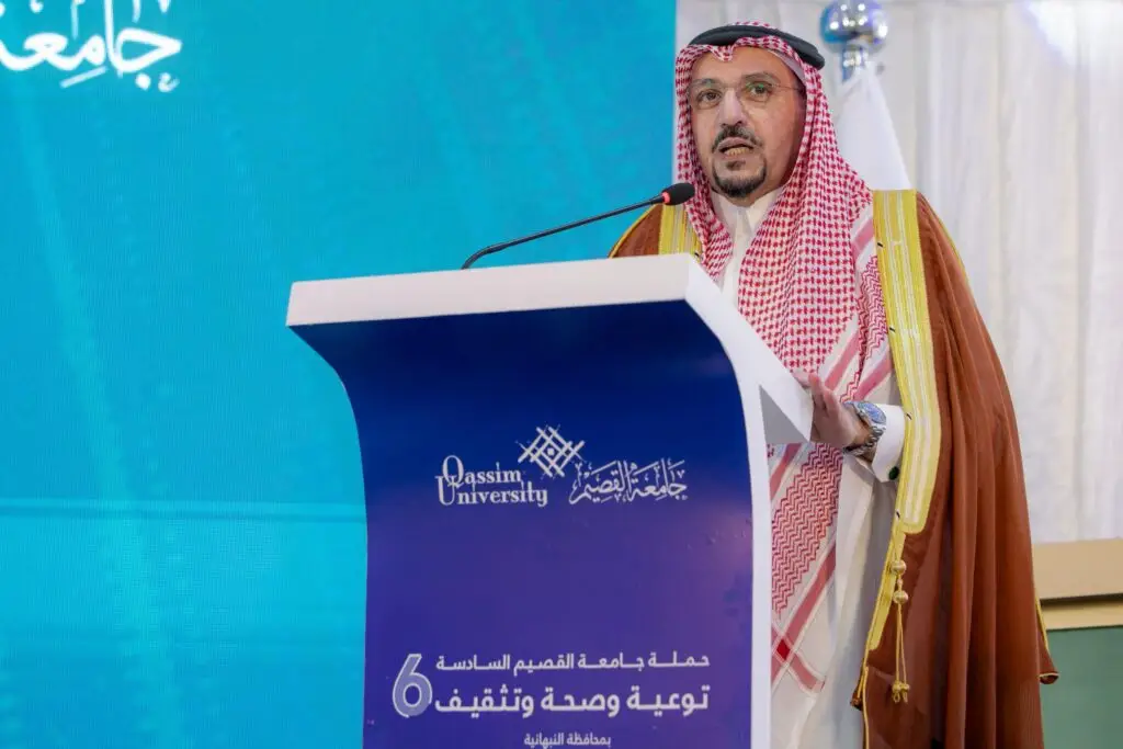 رجل مرتدياً الغترة والعقال والبشتت السعودي الرسمي أمام المنصة التي تحمل شعار جامعة القصيم، ليلقي كلمة خلال فعالية "حملة الجامعة الشاملة". تم تصميمها في شاشة زرقاء تحمل نصوص عربية لتشير إلى مقاطعة النبهانية، وتبرز الإشادة بجهود أمير منطقة القصيم وتكريمه ضمن برنامج رسمي.