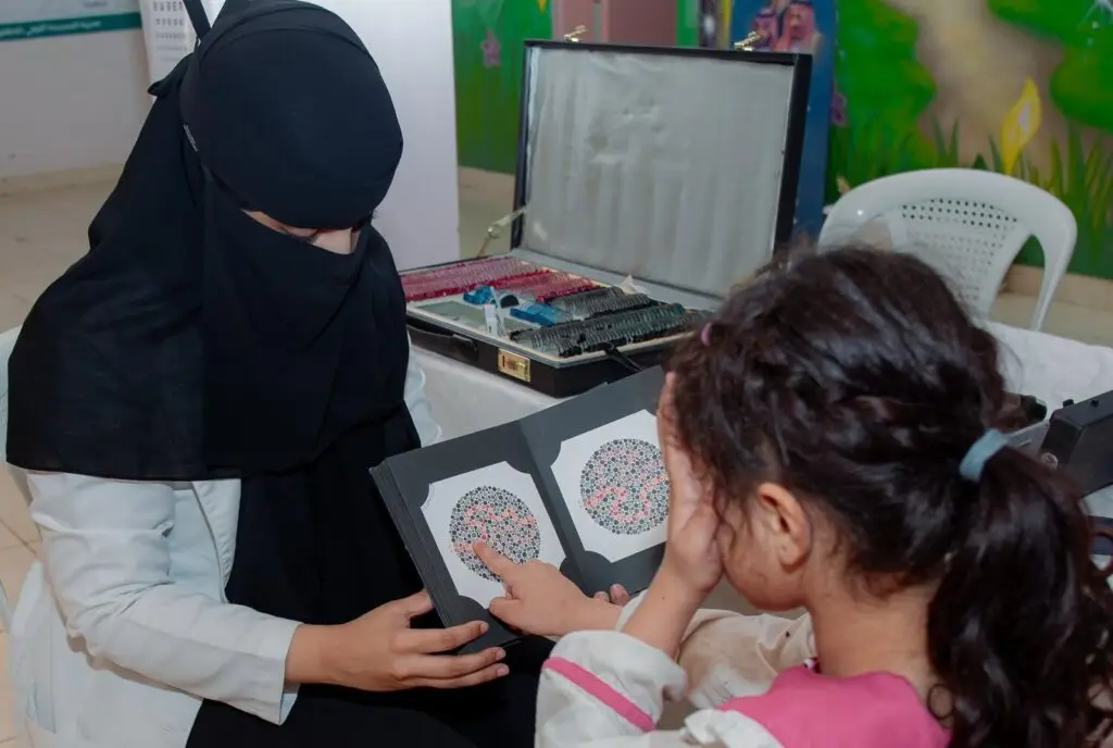 قامت الوقوف أمامنا اختبارًا لفحص الألوان للطفلة في مقاطعة النبهانية سيدة، وذلك في إطار فعالية توعوية لتعزيز الوعي بأهمية صحة العين، ولكن من جامعة القصيم. وقد شارك في نهاية الأسبوع عدد من الرجال بملابسهم التقليدية، من الشماغ أو الغترة والعقال والبشت السعودي. كما يأتي في مجاورة أدوات خاصة لفحص البصر واختبارات قياس النظر، مما يبرز الاهتمام بالجوانب العلمية والتنظيمية في هذا الحدث الصحي.