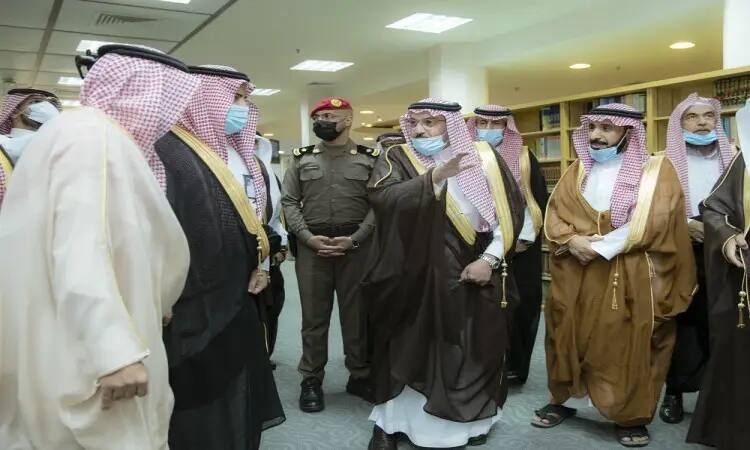 A group of men dressed in Saudi Arabian ghutra or shemagh with an aqal and a bisht, exchange a modern security room with a uniformed officer. It looks official to them, and the place is likely a library belonging to Qassim University, which is associated with the name of His Royal Highness Prince Dr. Faisal bin Meshal.