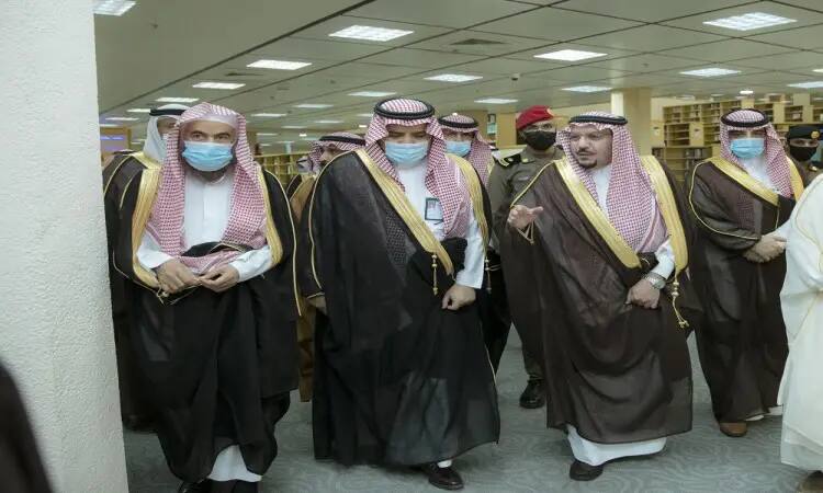 His Highness Dr. Faisal bin Meshal, accompanied by a group of men wearing the Saudi Arabian Ghutra or Amir al-Amir, Shaqal and Bisht, walks through the library of Qassim University, where he controls the bookshelves and lights in the background.