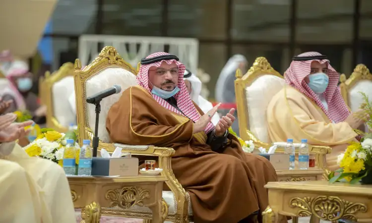A seated group of men dressed in the Ghutra or Shemagh and Eqal, as well as the Saudi Besht, on a plush in Qassim, Saudi Arabia. They are labeled to commemorate the event, and are dressed according to health measures. The tables are adorned with bouquets of fresh flowers, water bottles, and microbes, suggesting that their official purpose could be a connection to solar energy.