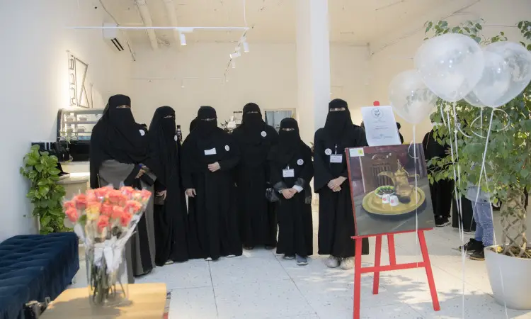 مجموعة من ارتداءن العباءات السوداء والبشوت السعودية، ويضعن الشماغات أو الغتر والعقال، تتن سوياً في قاعة حديثة ومضيئة في جامعة القصيم. إلى جانبهن لوحة شرف عروض معروضة على شماع وأصل ثابت، وعدد من البالونات تؤكد على الشرف العالمي للاحتفال بنادي كاليوم للغة العربية". وتضفي الجودة العالية على الموضوع بعناية لمسة راقية وأناقة على الوجه الرسمي.