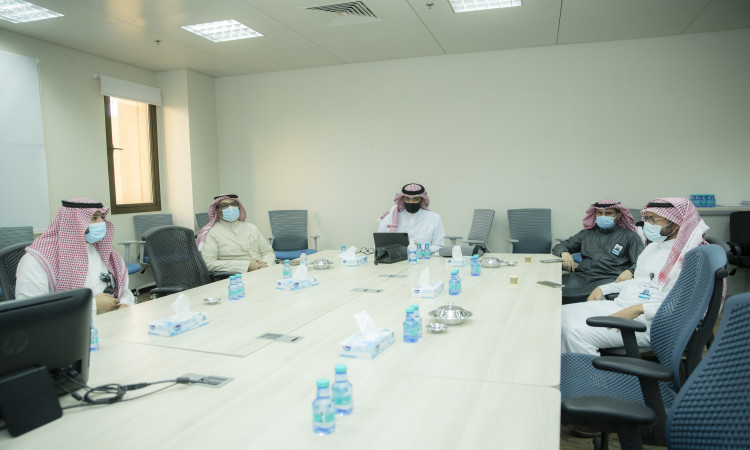 يجتمع ستة رجال حديثين الغترة أو الشماغ السعودي مع العقال والبشت السعودي، ويلتزمون بارتداء الكمامات الطبية، حول طاولة تلبي احتياجات أحد في مدينة الملك عبد الله الطبية في القصيم. أعلن جدول على الأجهزة وحاسب محمول وقوارير ماء وعلب مناديل ومقّم لليدين، بما في ذلك تأكيد التعاون الطبي والتغيير ضمن نظام الإعلان الرسمي في الجامعة.